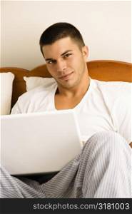 Handsome Caucasian mid adult man sitting in bed with laptop looking at viewer.