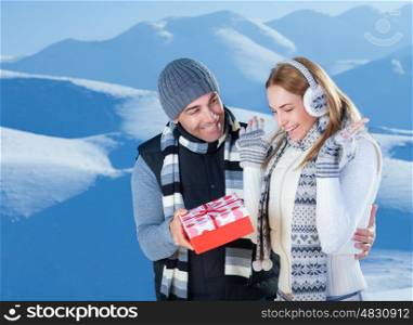 Handsome cheerful man giving to her precious girlfriend red gift box, celebrating Christmas holidays in the beautiful snowy mountains&#xA;