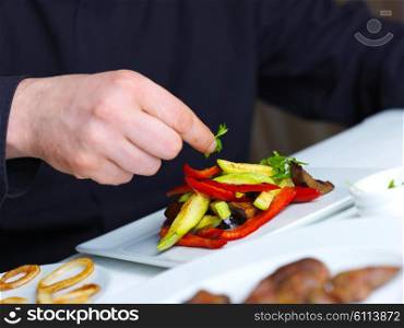 Handsome chef dressed in black uniform decorating tasty food in restaurant