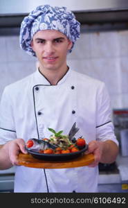 Handsome chef dressed in white uniform decorating pasta salad and seafood fish in modern kitchen