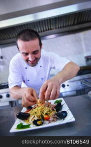 Handsome chef dressed in white uniform decorating pasta salad and seafood fish in modern kitchen