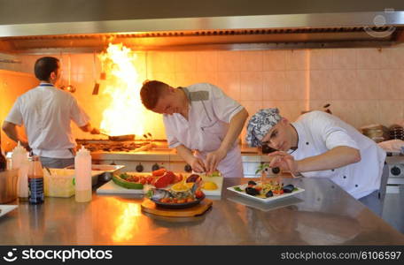 Handsome chef dressed in white uniform decorating pasta salad and seafood fish in modern kitchen