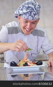 Handsome chef dressed in white uniform decorating pasta salad and seafood fish in modern kitchen