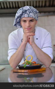 Handsome chef dressed in white uniform decorating pasta salad and seafood fish in modern kitchen