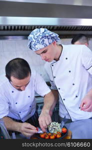 Handsome chef dressed in white uniform decorating pasta salad and seafood fish in modern kitchen