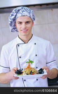 Handsome chef dressed in white uniform decorating pasta salad and seafood fish in modern kitchen