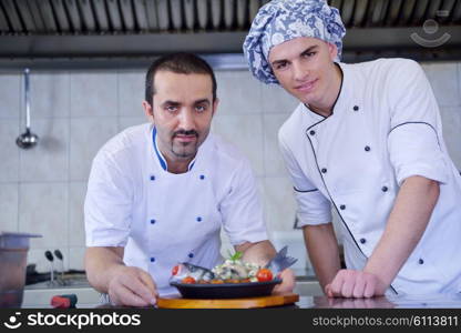 Handsome chef dressed in white uniform decorating pasta salad and seafood fish in modern kitchen