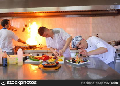 Handsome chef dressed in white uniform decorating pasta salad and seafood fish in modern kitchen