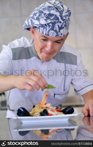 Handsome chef dressed in white uniform decorating pasta salad and seafood fish in modern kitchen