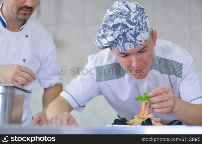 Handsome chef dressed in white uniform decorating pasta salad and seafood fish in modern kitchen