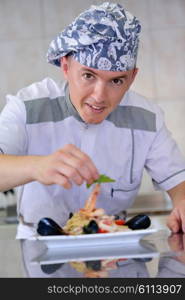 Handsome chef dressed in white uniform decorating pasta salad and seafood fish in modern kitchen