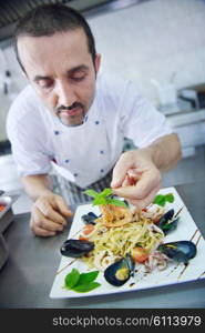 Handsome chef dressed in white uniform decorating pasta salad and seafood fish in modern kitchen