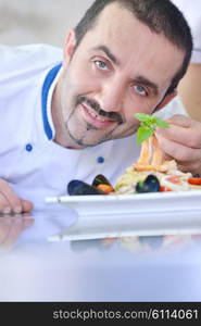 Handsome chef dressed in white uniform decorating pasta salad and seafood fish in modern kitchen