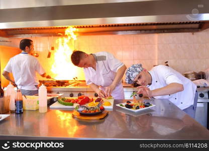 Handsome chef dressed in white uniform decorating pasta salad and seafood fish in modern kitchen