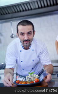 Handsome chef dressed in white uniform decorating pasta salad and seafood fish in modern kitchen