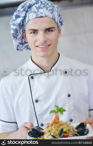 Handsome chef dressed in white uniform decorating pasta salad and seafood fish in modern kitchen