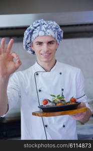 Handsome chef dressed in white uniform decorating pasta salad and seafood fish in modern kitchen