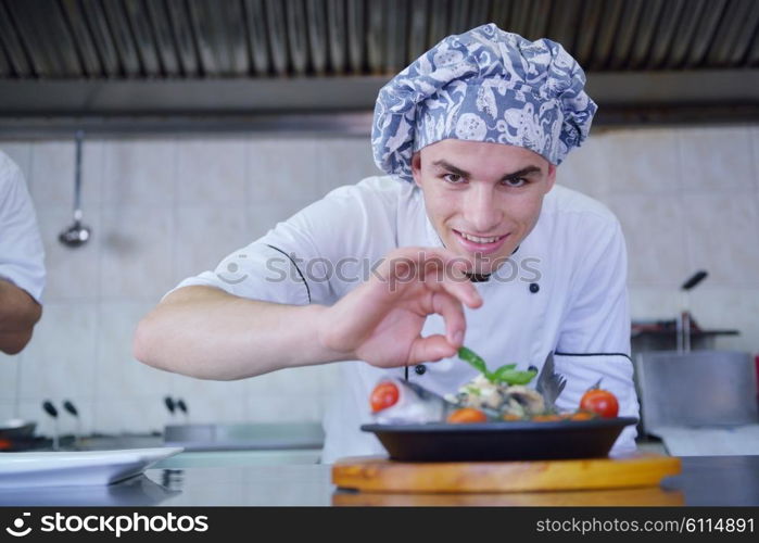 Handsome chef dressed in white uniform decorating pasta salad and seafood fish in modern kitchen