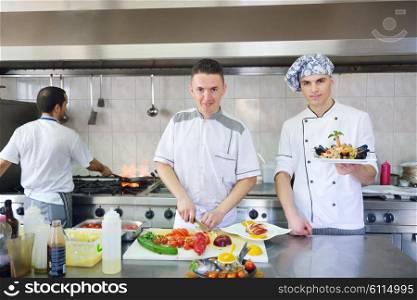 Handsome chef dressed in white uniform decorating pasta salad and seafood fish in modern kitchen