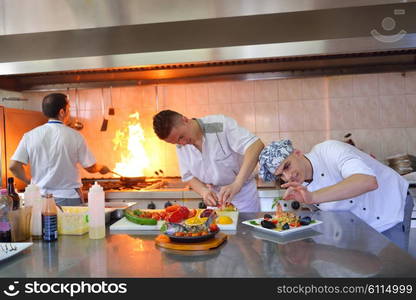 Handsome chef dressed in white uniform decorating pasta salad and seafood fish in modern kitchen