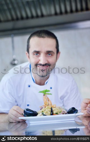 Handsome chef dressed in white uniform decorating pasta salad and seafood fish in modern kitchen