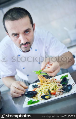 Handsome chef dressed in white uniform decorating pasta salad and seafood fish in modern kitchen