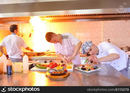 Handsome chef dressed in white uniform decorating pasta salad and seafood fish in modern kitchen