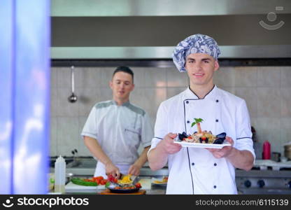 Handsome chef dressed in white uniform decorating pasta salad and seafood fish in modern kitchen