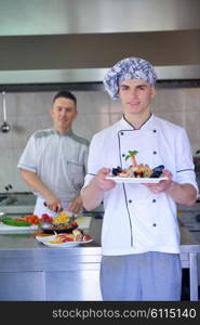 Handsome chef dressed in white uniform decorating pasta salad and seafood fish in modern kitchen