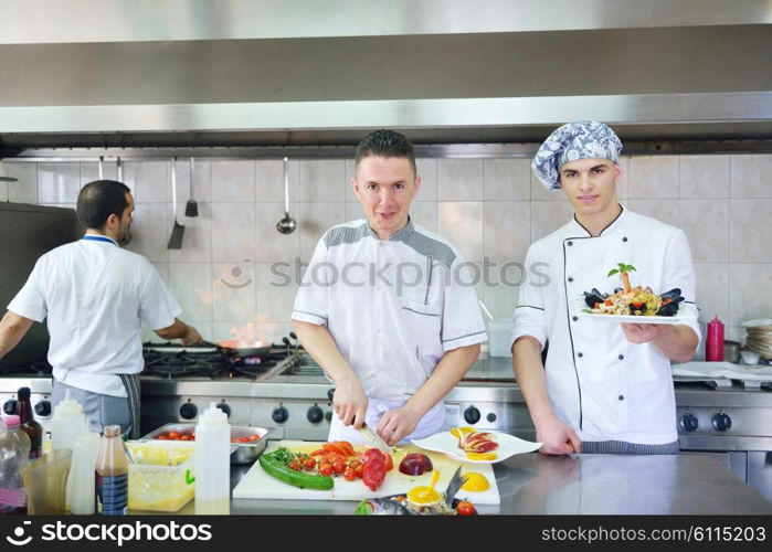 Handsome chef dressed in white uniform decorating pasta salad and seafood fish in modern kitchen