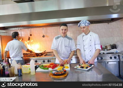 Handsome chef dressed in white uniform decorating pasta salad and seafood fish in modern kitchen