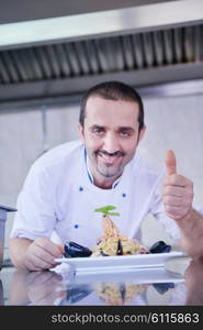 Handsome chef dressed in white uniform decorating pasta salad and seafood fish in modern kitchen