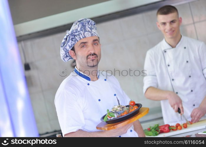 Handsome chef dressed in white uniform decorating pasta salad and seafood fish in modern kitchen