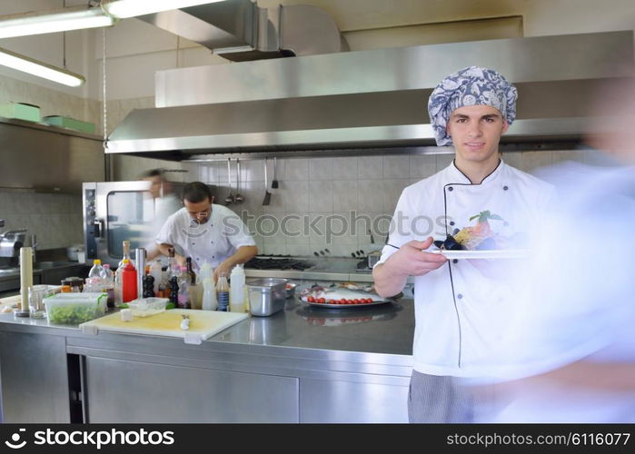 Handsome chef dressed in white uniform decorating pasta salad and seafood fish in modern kitchen