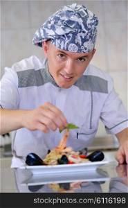 Handsome chef dressed in white uniform decorating pasta salad and seafood fish in modern kitchen