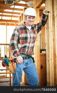 Handsome construction worker working on a frame house, with his tools.