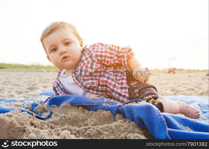 Handsome curious child lying on sand on the beach playing, sunny day.