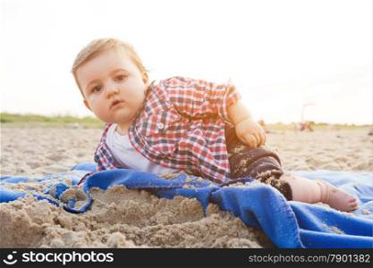Handsome curious child lying on sand on the beach playing, sunny day.
