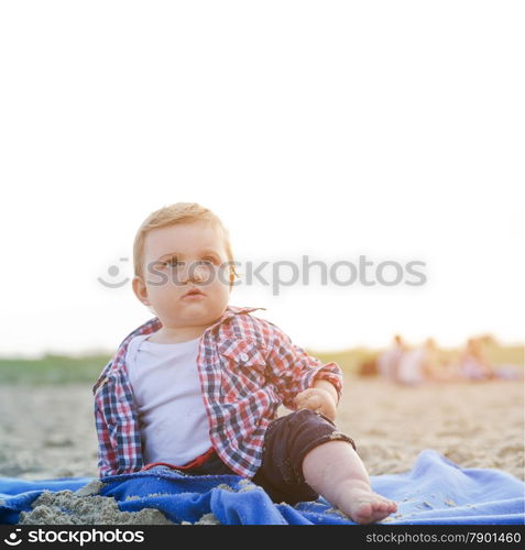 Handsome curious child sitting on sand on the beach looking at the sky at sunny day.