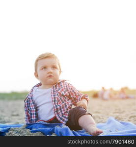 Handsome curious child sitting on sand on the beach looking at the sky at sunny day.