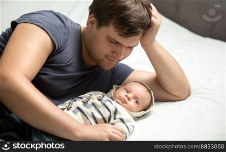 Handsome daddy hugging baby boy lying on bed