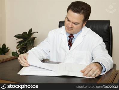 Handsome doctor at his desk going over a patient&rsquo;s chart.