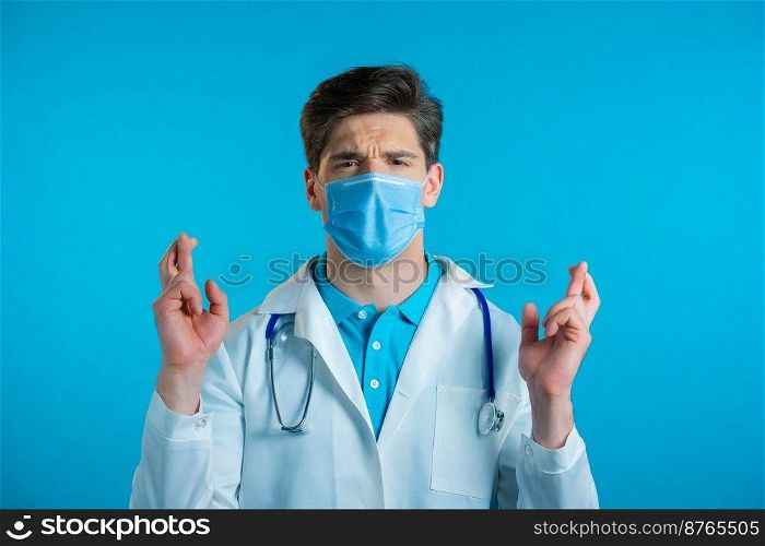 Handsome doctor in mask praying over blue background. Man begging someone satisfy his desires, help with. High quality photo. Handsome doctor in mask praying over blue background. Man begging someone satisfy his desires, help with.