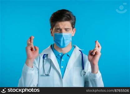 Handsome doctor in mask praying over blue background. Man begging someone satisfy his desires, help with. High quality photo. Handsome doctor in mask praying over blue background. Man begging someone satisfy his desires, help with.