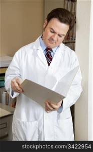 Handsome doctor in the file room reading a patient&rsquo;s chart.