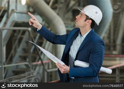handsome engineer pointing at pipes in a factory