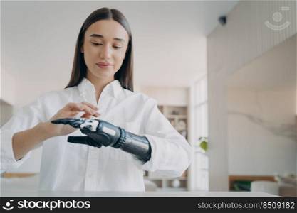 Handsome european girl has high tech mechanical arm prosthesis. Happy handicapped girl is setting the prosthesis functions at home. Modern orthopedic technology and invention for wellbeing.. Happy handicapped girl is setting the prosthesis functions at home. Modern orthopedic technology.