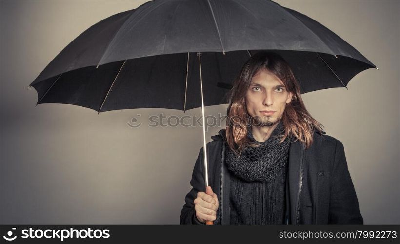 Handsome fashion man portrait wearing black coat.. Portrait of handsome fashionable man wearing black coat and scarf holding umbrella. Young guy posing in studio. Winter or autumn fashion. Instagram filter.