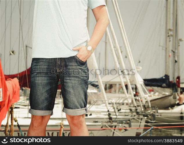 Handsome fashion man tourist on pier in port with yachts. Guy enjoying summer travel vacation by sea.