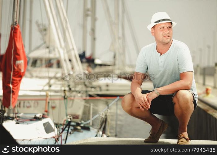 Handsome fashion man tourist on pier in port with yachts. Guy enjoying summer travel vacation by sea.